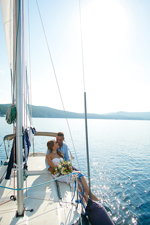 Amorous bride and groom traveling by yacht on sunny day