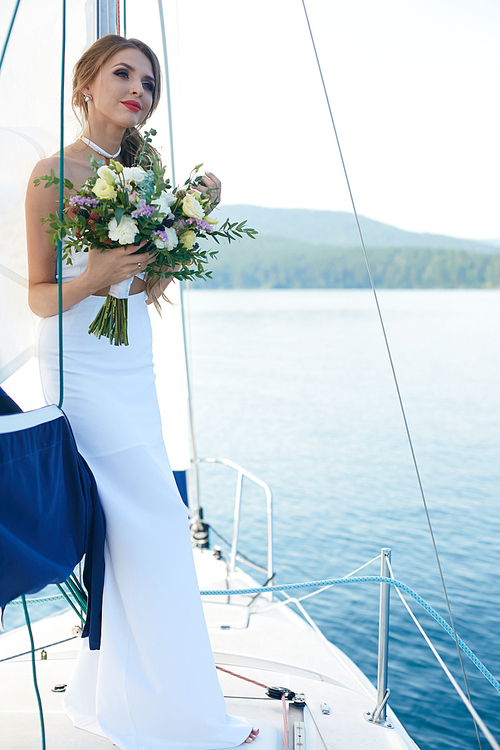 Attractive bride in white wedding dress floating by yacht