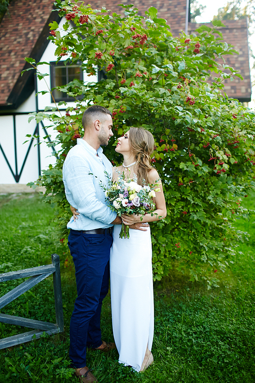 Young bride and groom standing by green tree in natural environment