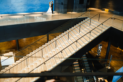 Staircase and escalator inside modern building with newlyweds on top floor