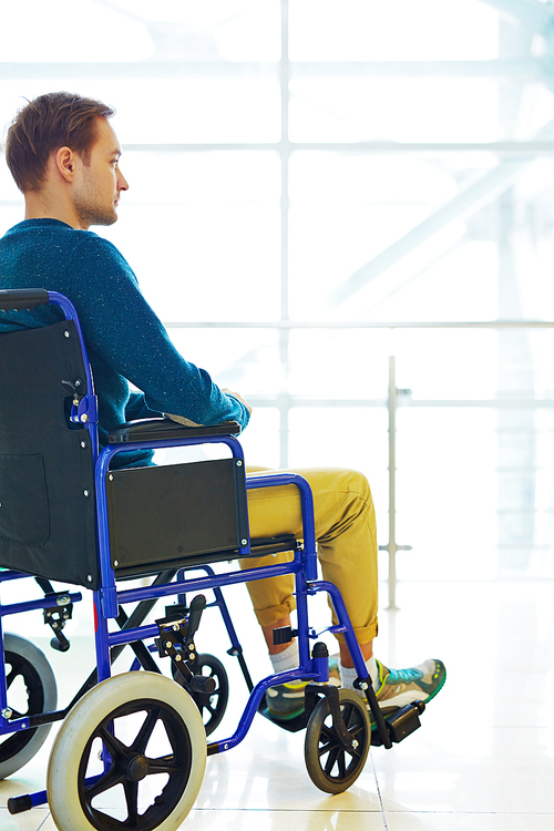 Side view of young man sitting in wheelchair and looking into the distance thoughtfully