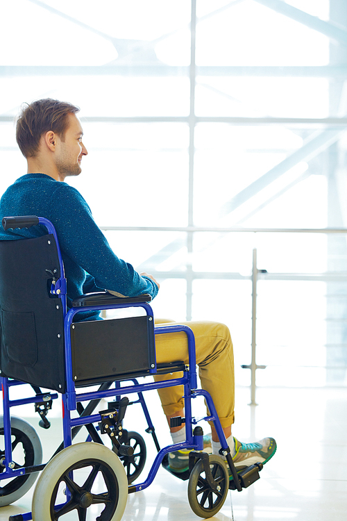 Side view of young man sitting in wheelchair, looking at someone and smiling brightly