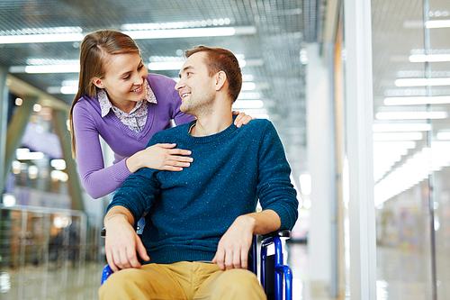 Portrait of smiling young woman looking at her disabled boyfriend in wheelchair with love in shopping mall
