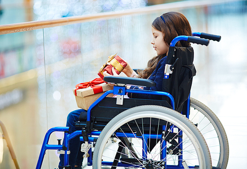 Side-view of disabled child in wheelchair looking at gift-box
