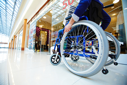 Disabled shopper moving in wheelchair along departments in the mall