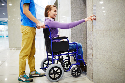 assistant and handicapped young woman in . waiting for elevator, she pressing button by herself and smiling
