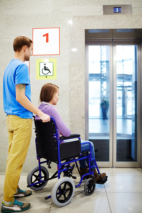 physically impaired young woman in . and her assistant waiting for elevator in shopping mall