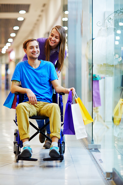 handicapped young man in . having good time with his loving girlfriend in mall, walking with shopping bags and smiling cheerfully