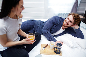 Happy young man lying in bed and talking to wife