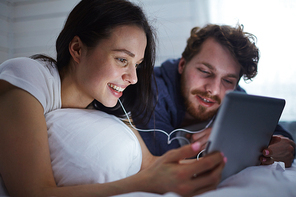 Modern young couple watching movie in touchpad while lying in bed