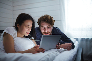 Amorous couple watching movie or networking in bed