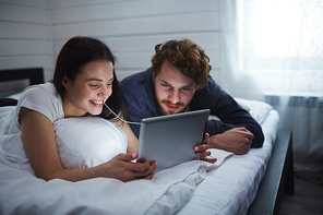 Restful couple with touchpad watching movie in bed