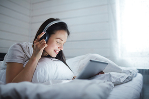 Girl with headphones and touchpad listening to music in bed