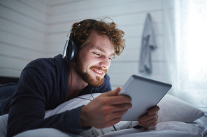 Happy guy with touchpad watching movie in bed