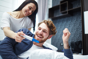 Happy young man looking at pregnancy test being shown by his wife