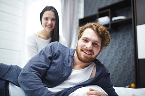 Happy man lying in bed with his wife on background