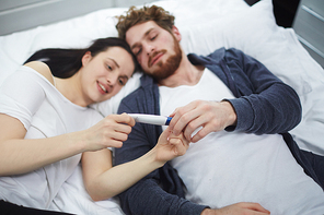 Young couple holding pregnancy test while lying in bed