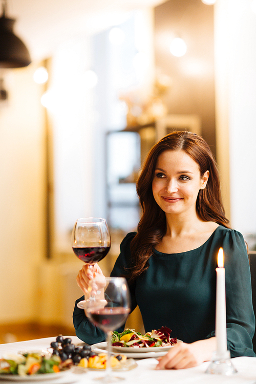 Happy young female with glass of red wine sitting in restaurant