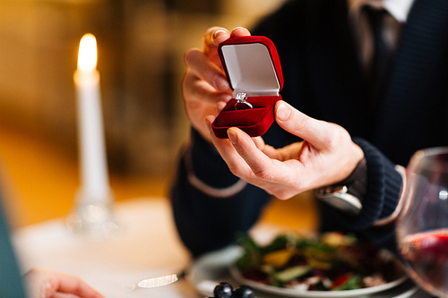 Young man showing his girlfriend red velvet box with engagement ring