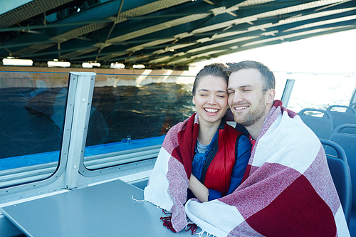 Laughing man and woman wrapped in plaid traveling by motorship