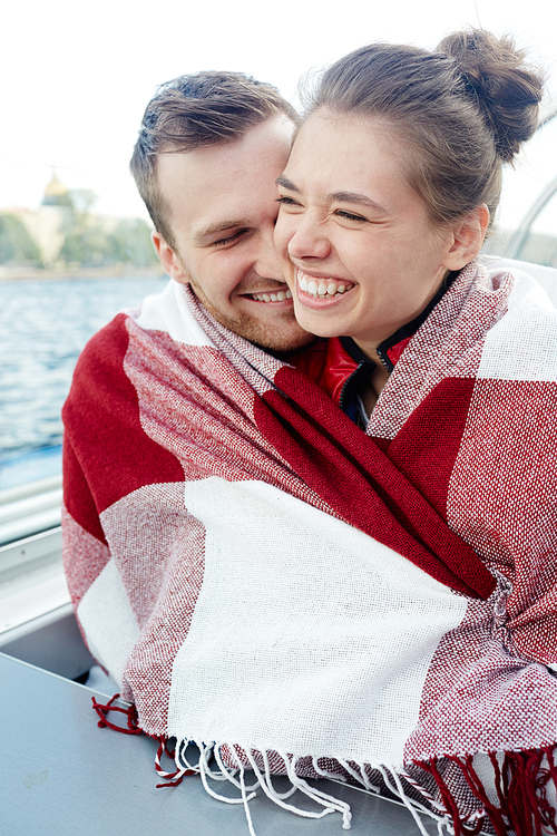 Joyful couple in embrace wrapped in plaid