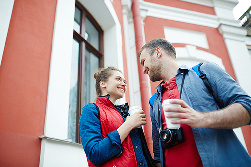 young man and woman with hot drinks spending leisure in urban