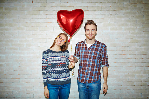 Happy couple holding symbol of love - red heart-shaped balloon