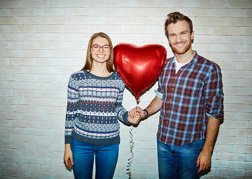 Romantic young couple holding red balloon in form of heart
