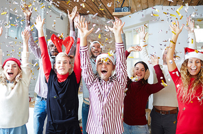 Carefree friends with raised hands enjoying Christmas party in traditional Santa caps