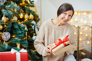 Retired woman opening giftbox with surprise on Christmas evening