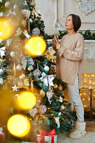 Reteired woman in homewear looking at firtree while decorating it on Christmas evening