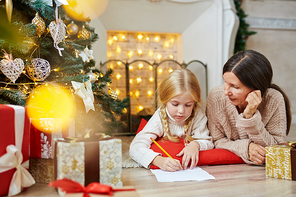 Cute little girl writing letter to Santa on xmas night with her grandmother near by