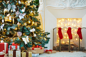 Decorated firtree, xmas gifts and red socks on fireplace in empty room