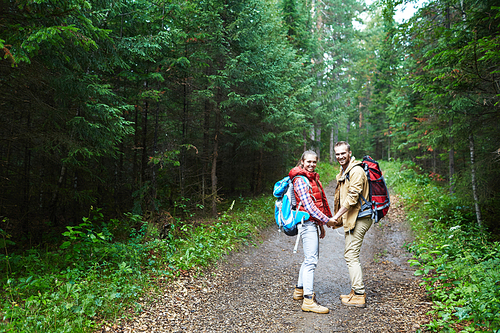 Happy young couple with backpacks having trip in the forest on rainy day