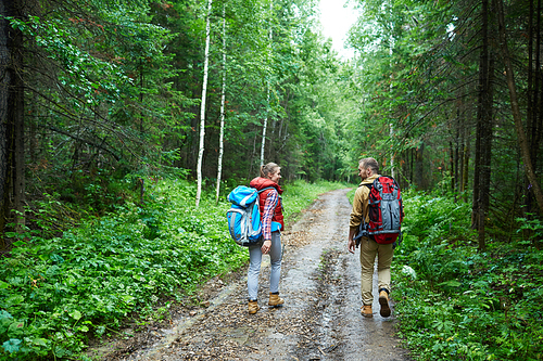 Modern couple with backpacks having walk in the forest