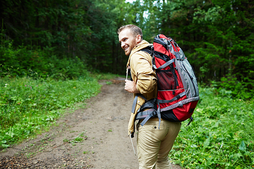 Happy young man with backpack looking back while hiking