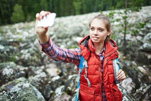 Pretty girl making selfie on background of big stones covered by moss during trip
