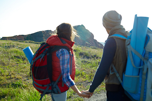 Back view image of young tourist couple looking away holding hands with focus on mountain far ahead