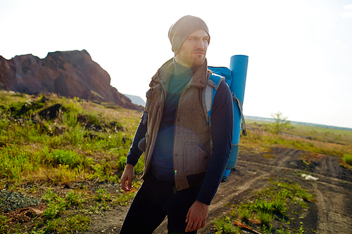 Model shot in with lens flare : adventurous handsome hiker wearing fashionable active outwear  traveling in lowland of mountains with backpack