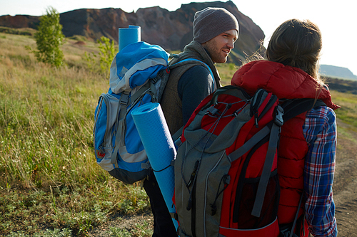 Young couple with big tourist backpacks travelling together in exploring lowland of mountains