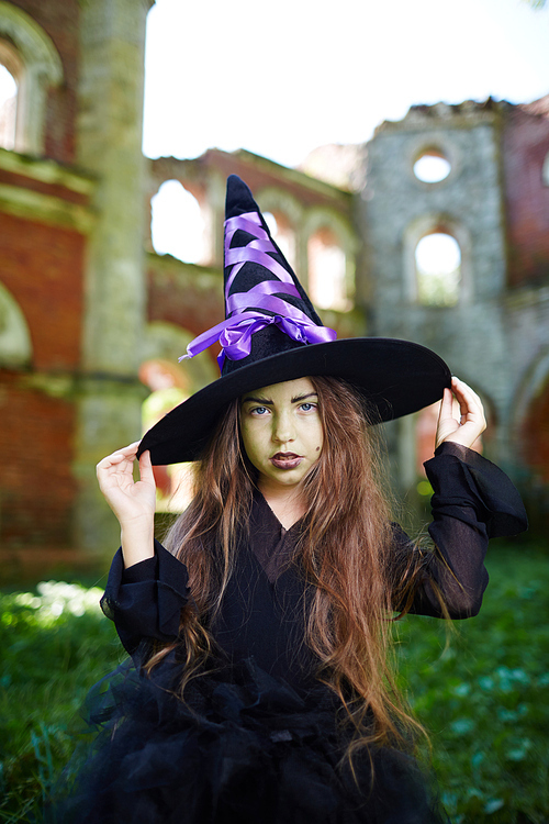 Cute girl with long hair wearing black dress and witch hat during outdoor halloween party