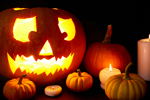 Ripe pumpkins surrounded by burning candles and carved jack-o-lantern