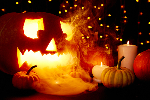 Sparkling Halloween background with burning candles and smoke over pumpkins