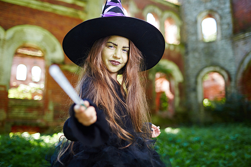 Little witch with magic stick making halloween trick upon you