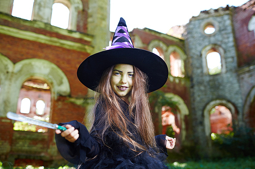 Cute little witch in halloween attire shaking by magic-wand