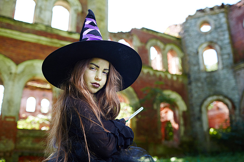 Sneaky little witch with magic wand  against shabby ruins