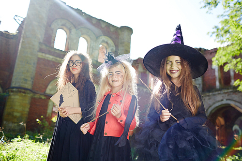 Girls in halloween costumes holding magic-sticks and book of spells