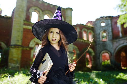 Sulky little in black attire and hat holding book and magic stick