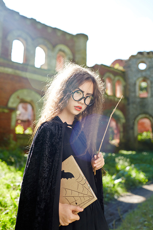 Asian girl with book and magic stick wearing black warlock