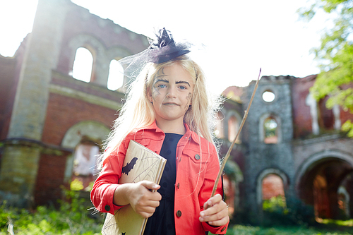 Blonde girl with halloween book and magic wand  by ruins of ancient fortress
